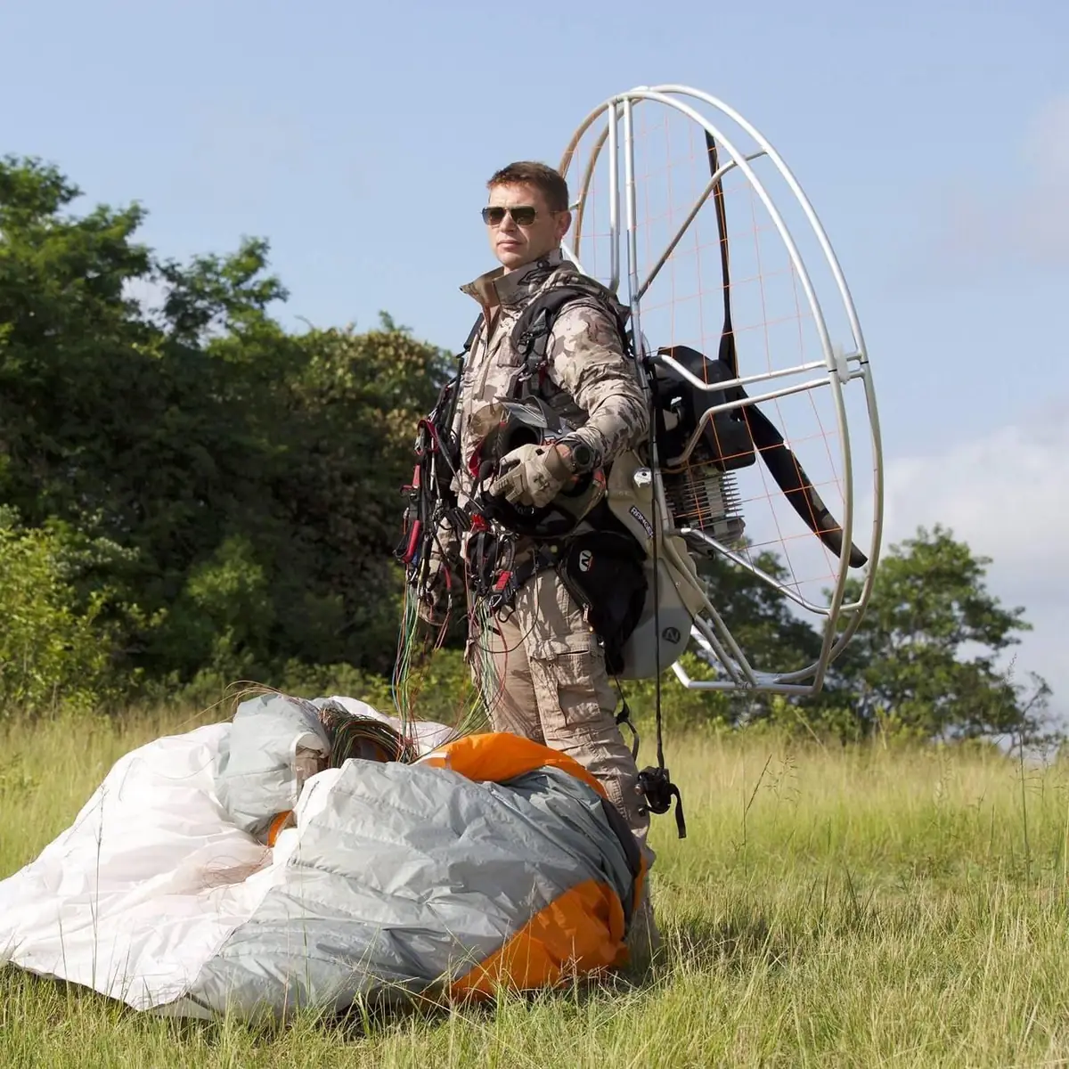 Eugene Cussons standing with a Nirvana paramotor and a wing on the ground in a grass field