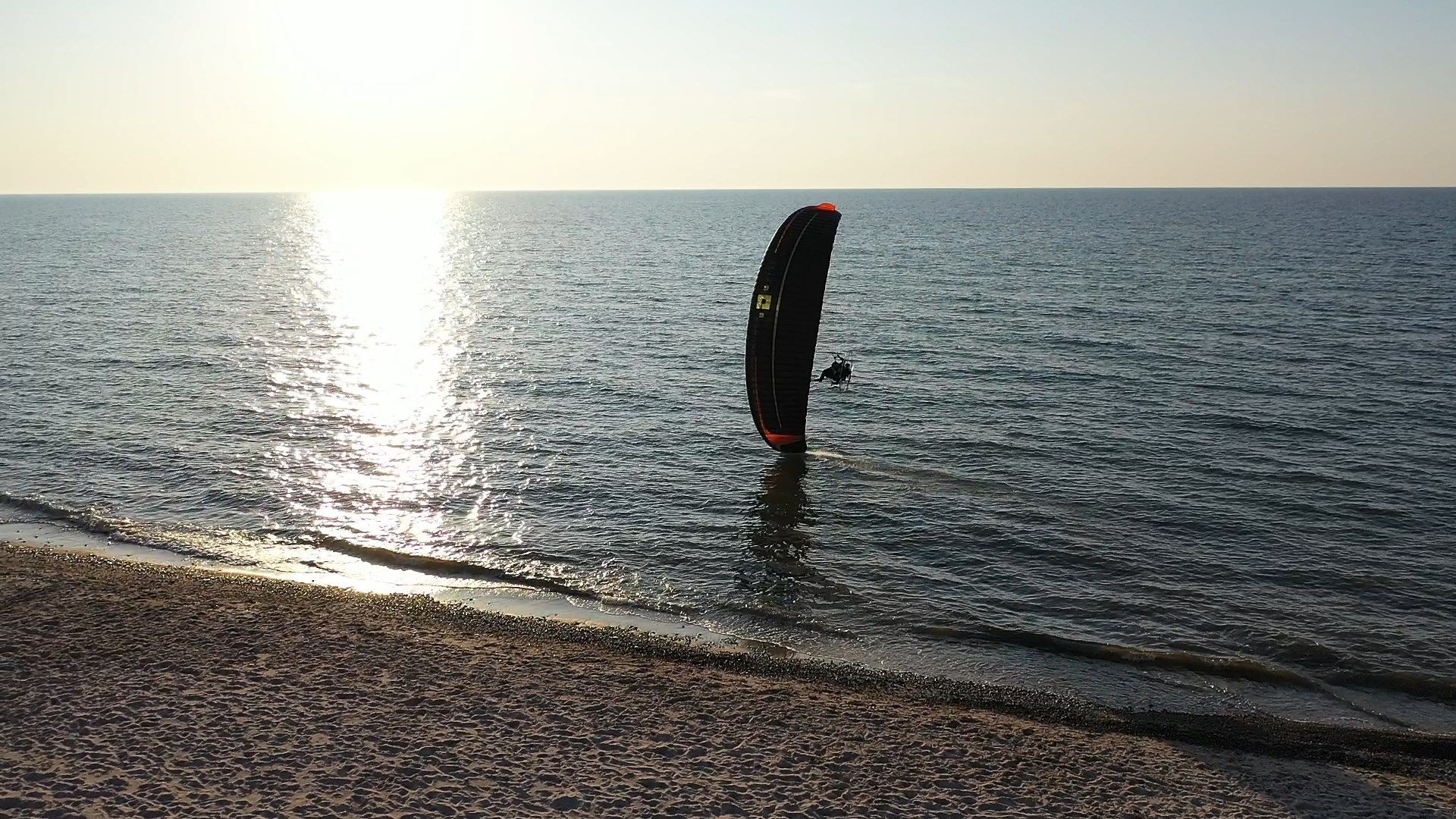 A paramotor wing standing at the water's edge on a beach at sunset