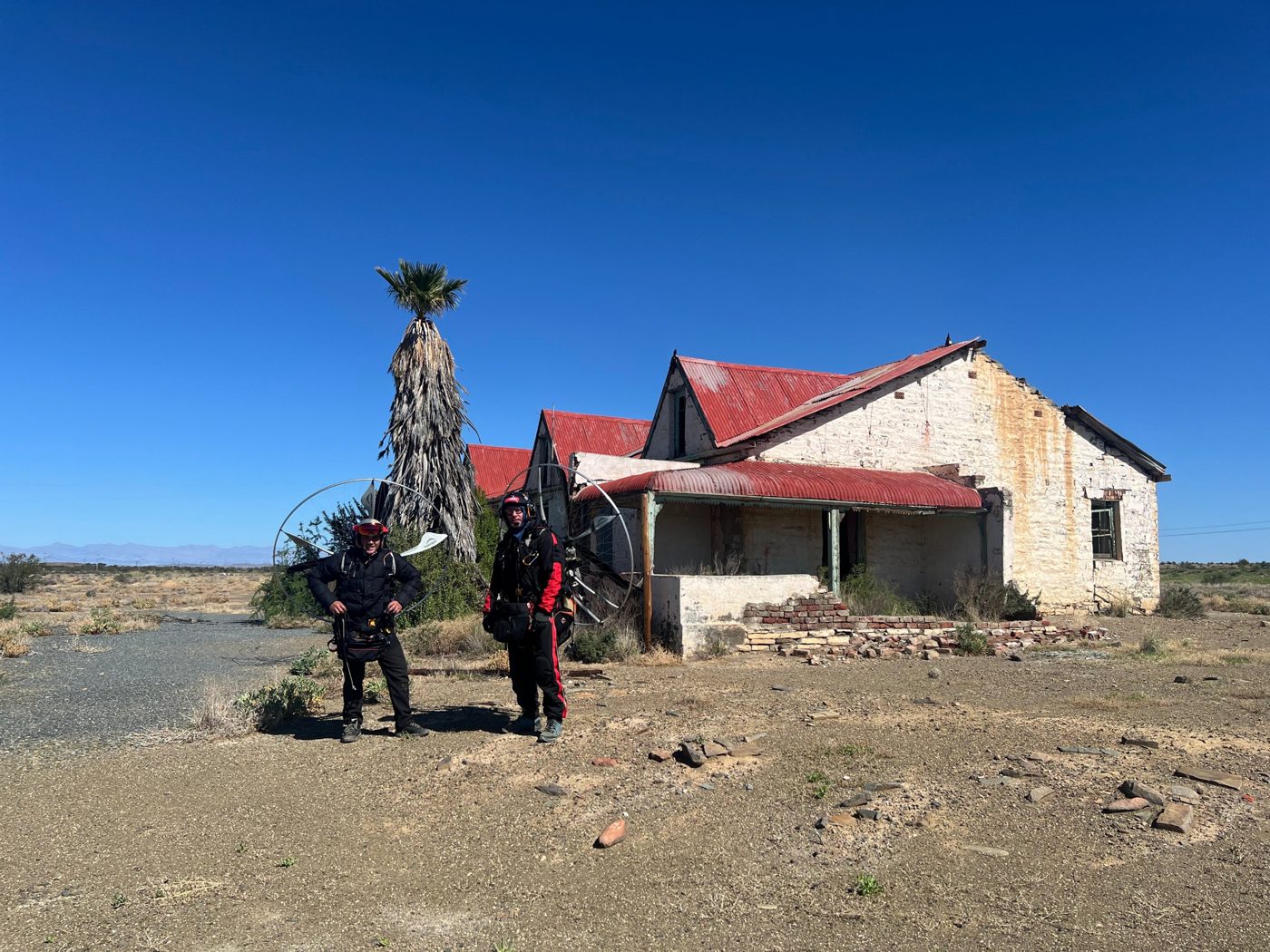 Two paramotor pilots in front of an old Karoo farmhouse