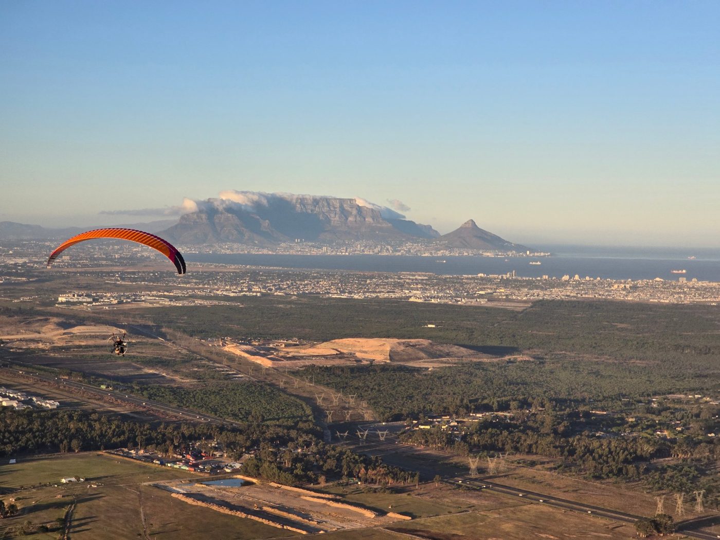A paramotor pilot flying towards Table Mountain and Cape Town
