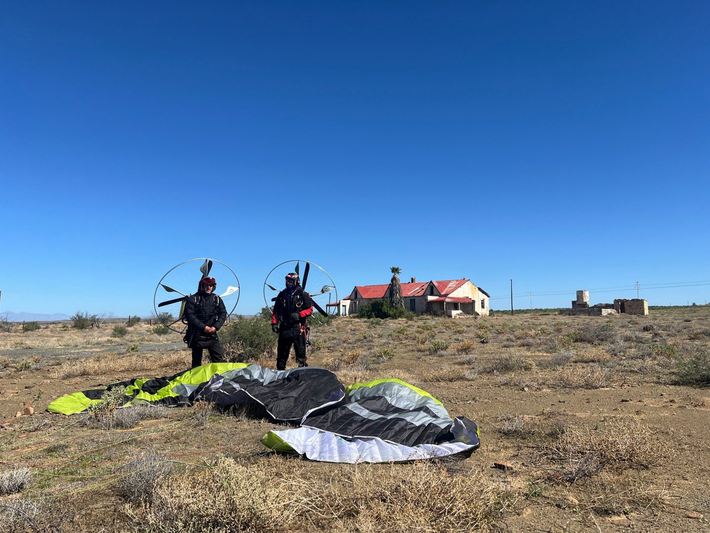 Two pilots with their paramotors beside wings laid out near the Karoo farmhouse