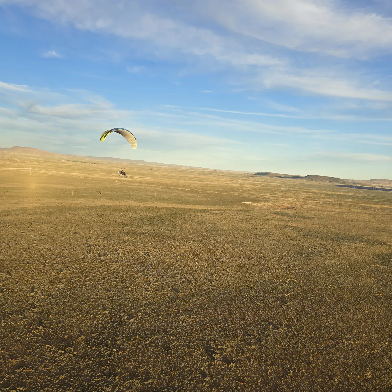 A paramotor flying low over open golden veld on Day 2