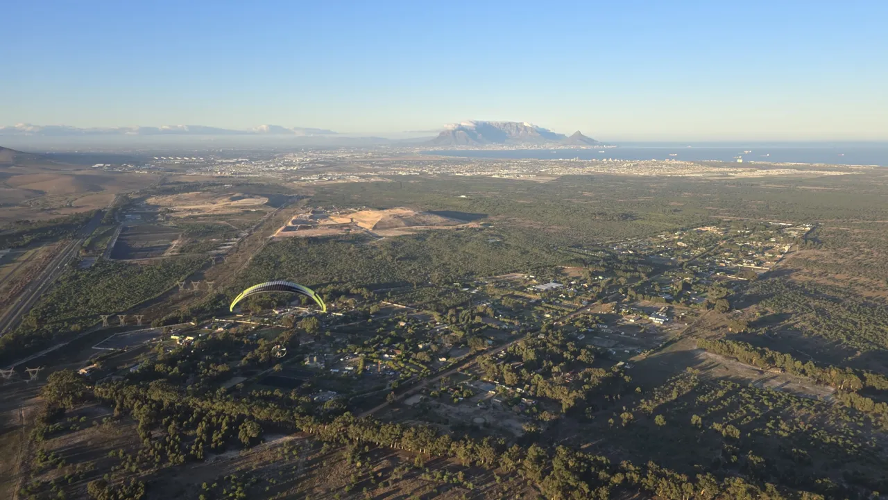 A paramotor wing over the Cape Town coast with Table Mountain on the horizon, seen from the air on Day 5