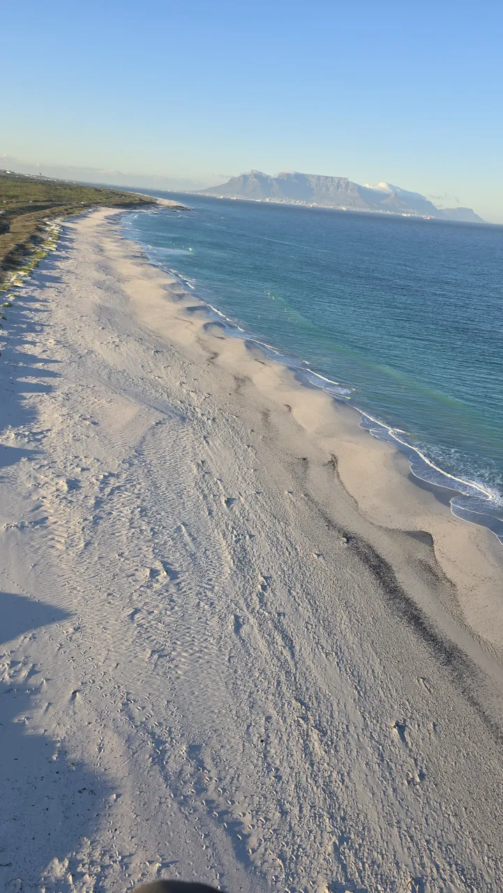 A long white beach and turquoise sea with Table Mountain in the distance, seen from the air on Day 5