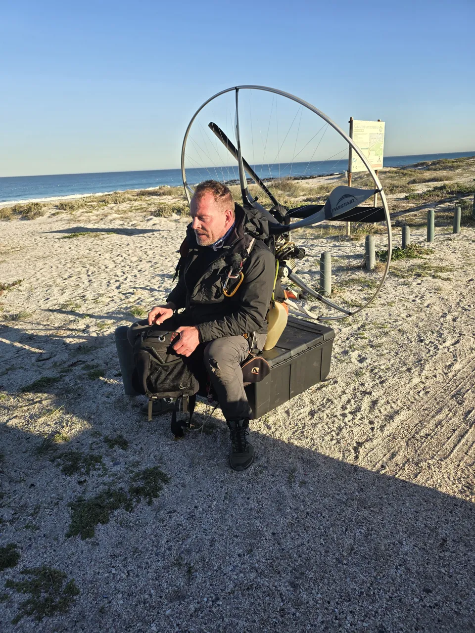 A pilot sitting on his paramotor on the beach after the last flight on Day 5