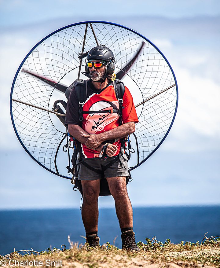 Paramotor pilot in sunglasses and headset standing on a cliff edge with the ocean behind