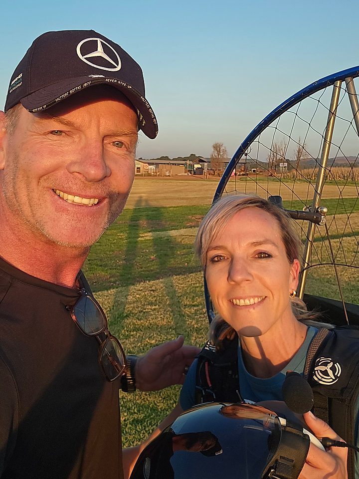 Instructor and student pilot smiling at sunset beside a paramotor after a qualifying flight