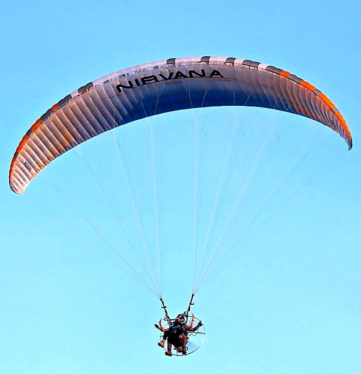 A Nirvana tandem wing flying in a clear blue sky with two people below
