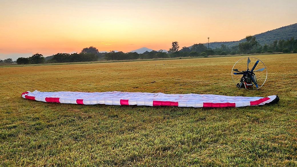 A paramotor and wing laid out on a grass field at sunrise