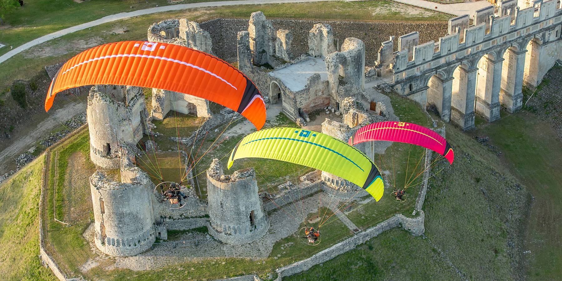Three paramotor wings flying over a ruined castle